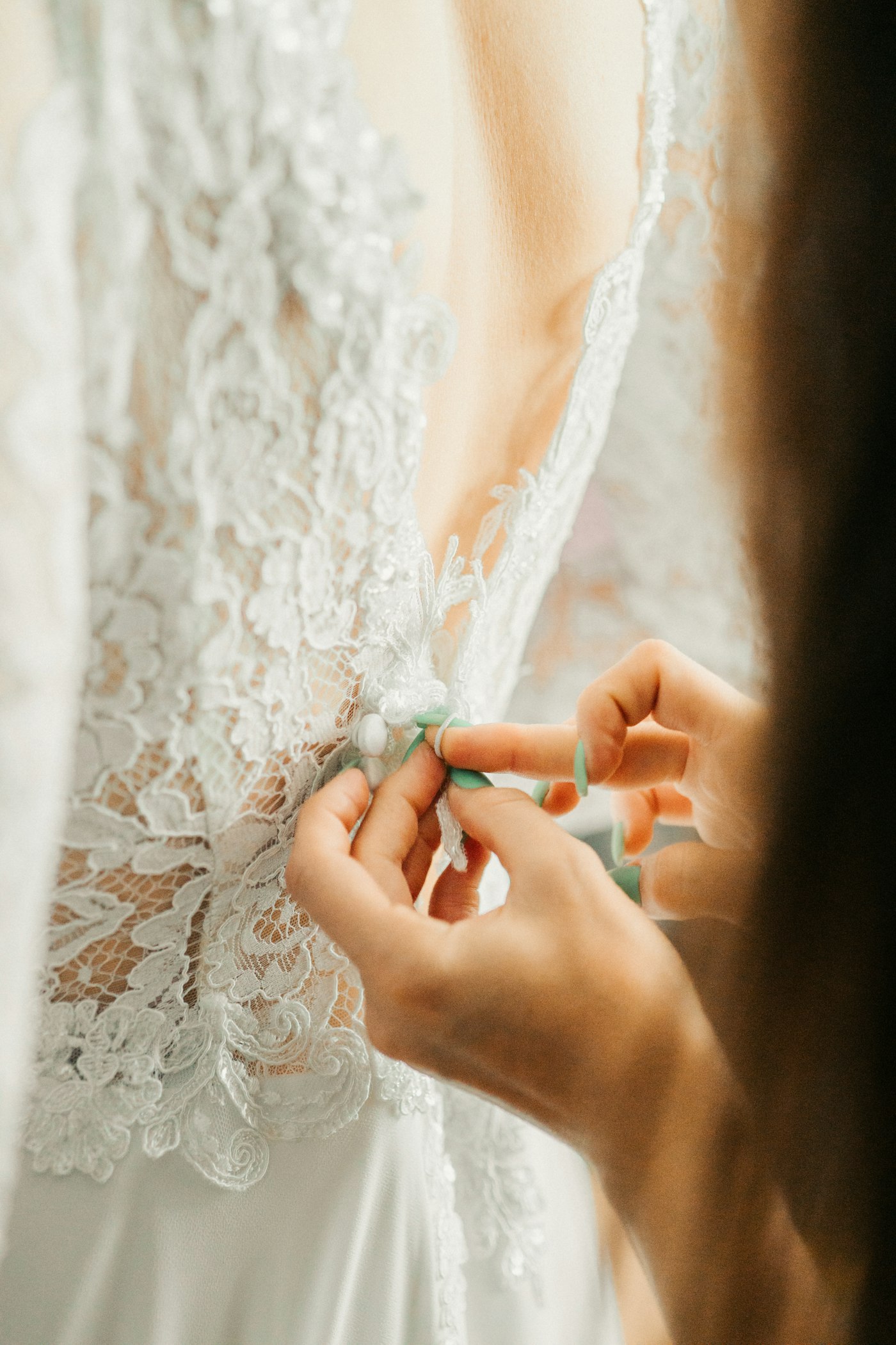 A dressmaker’s hands fastening the lace back of a bespoke bridal gown