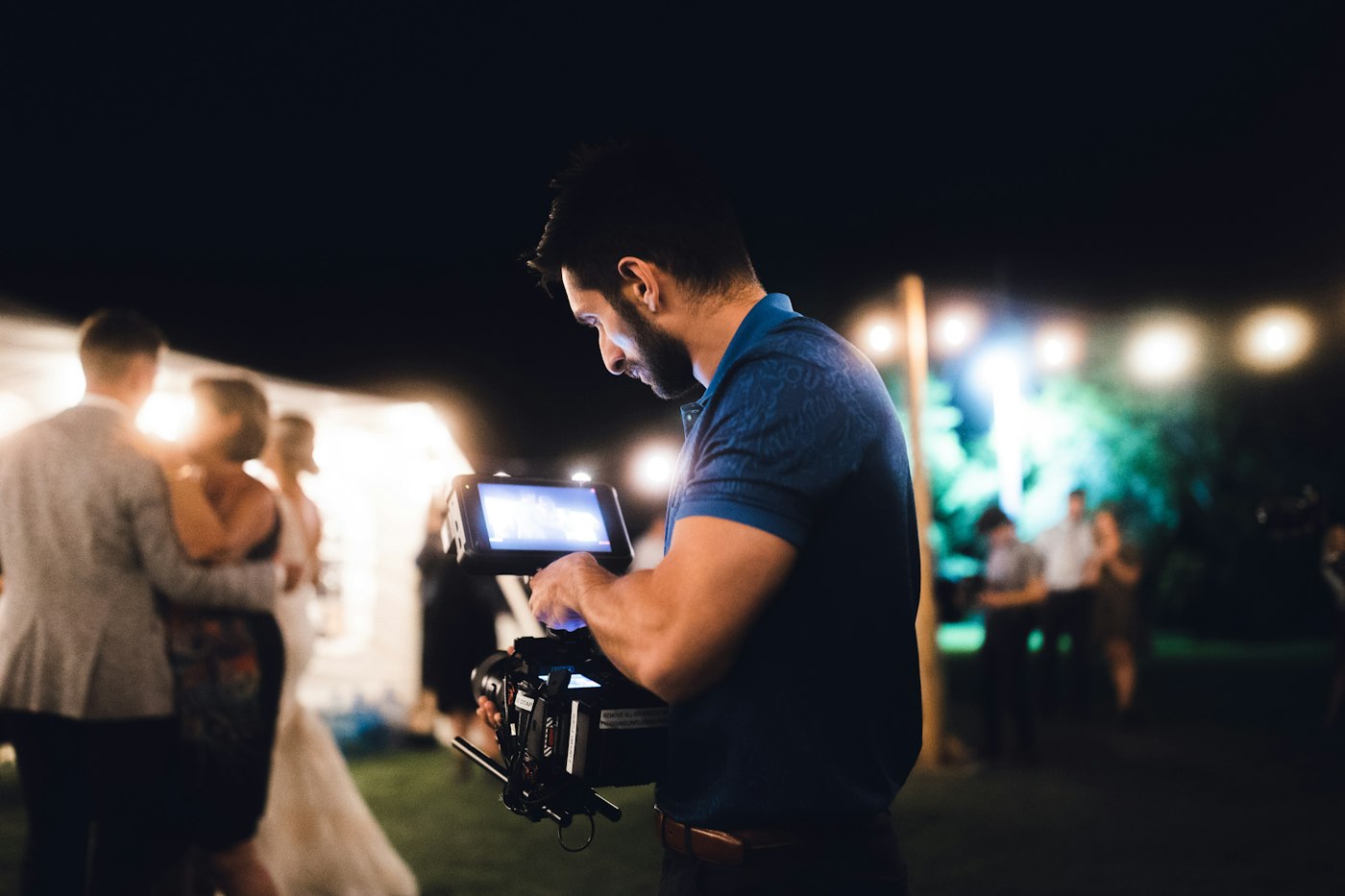 Videographer filming a couple with a handheld camera at a night-time wedding reception